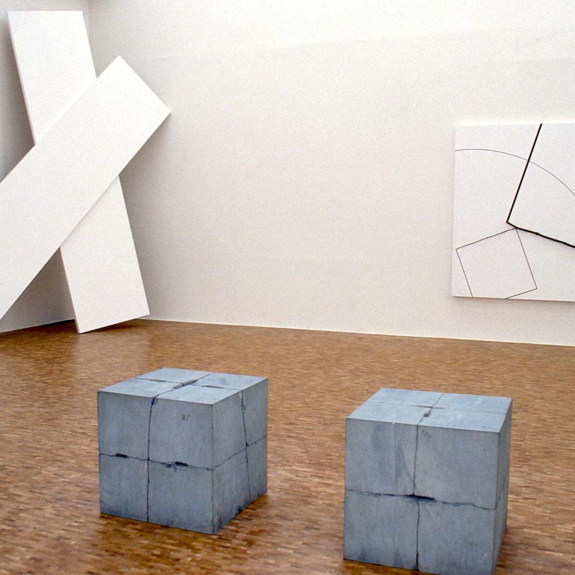 Salle d'exposition avec tableau/installation aux murs et cubes au sol.