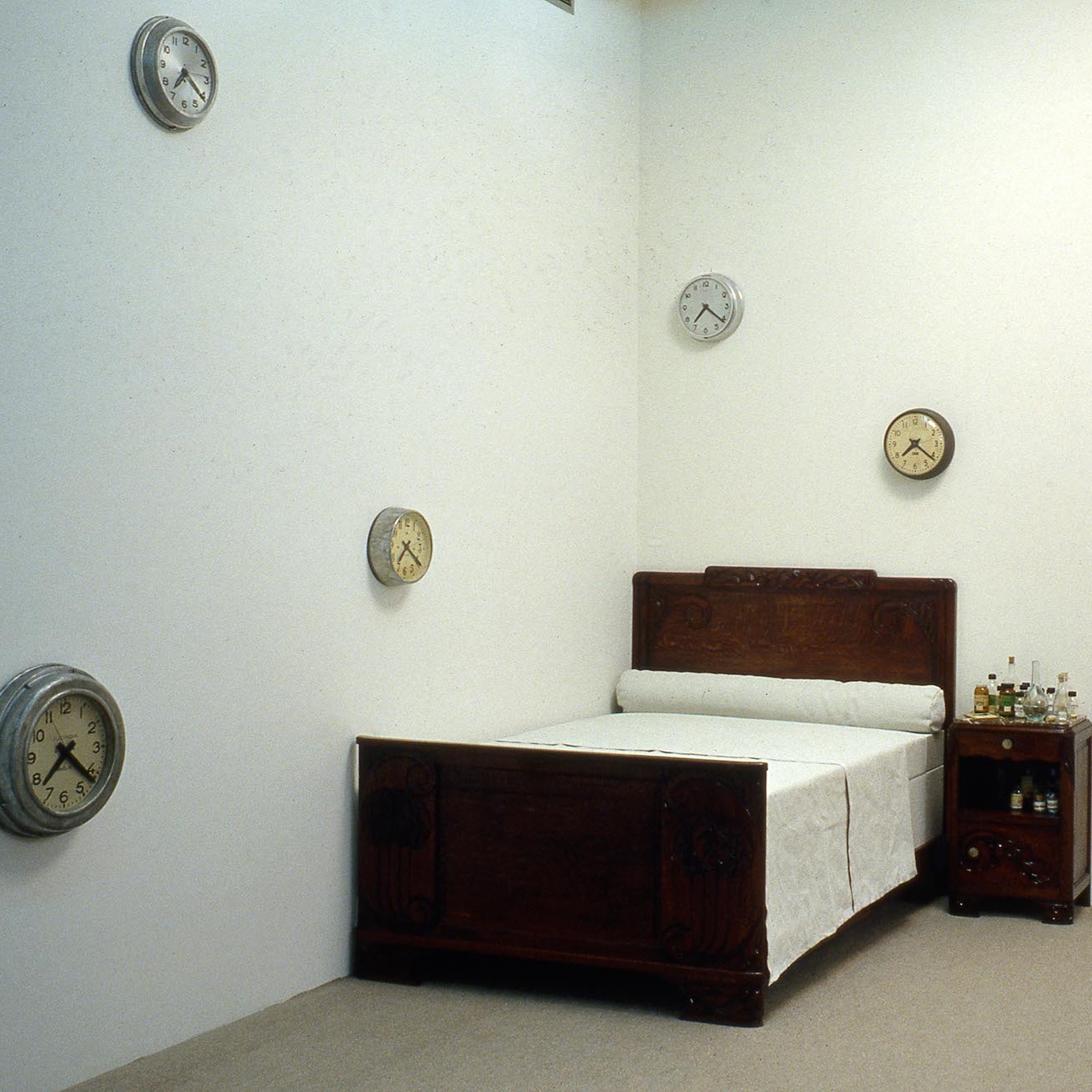 Installation d'horloges aux murs, d'un lit et d'une table de chevet au sol.