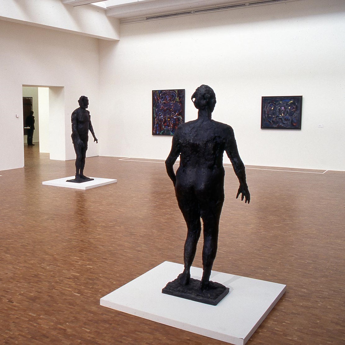 Salle d'exposition, sculptures aux centres et tableaux aux murs.