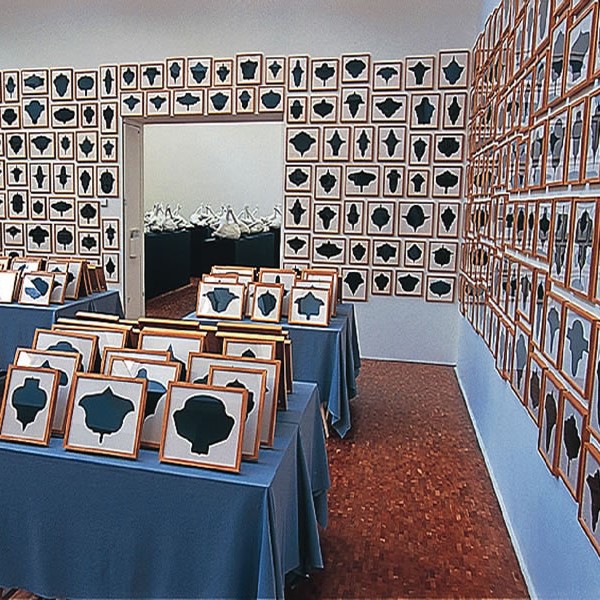 Accumulation de tableaux sur tables et murs d'une salle d'exposition.