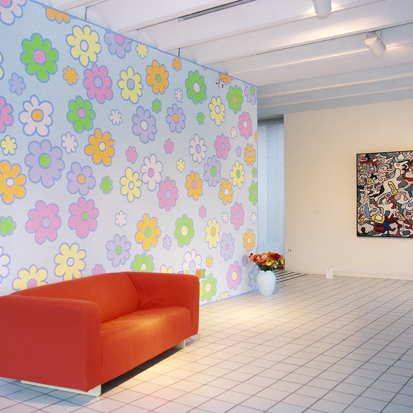 Salle d'exposition avec canapé rouge, mur motif fleur et tableau.