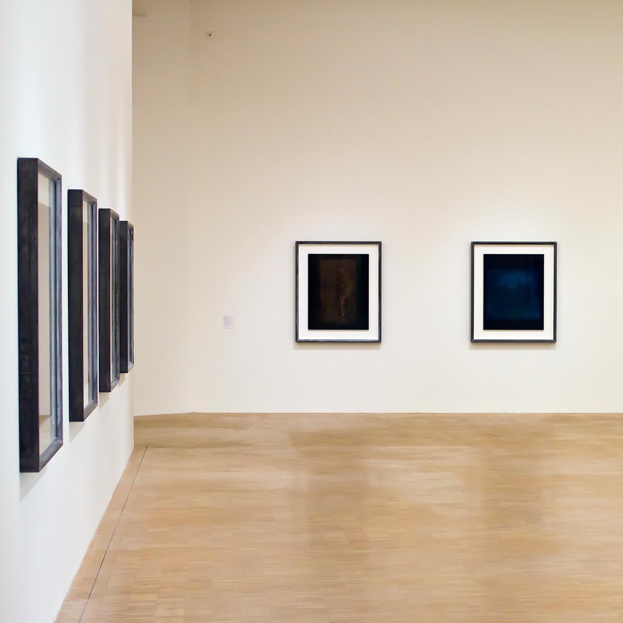 Salle d'exposition avec toiles aux murs foncées.