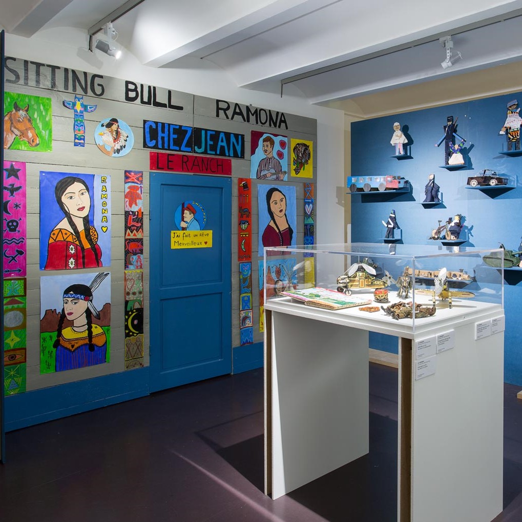 Salle d'exposition avec vitrine en son centre et œuvres aux murs.