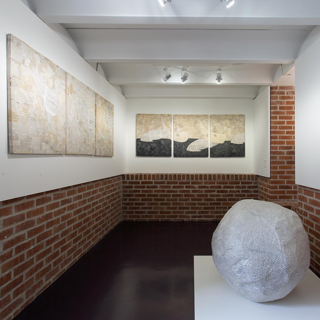 Salle d'exposition avec toiles aux murs et sculpture au sol.