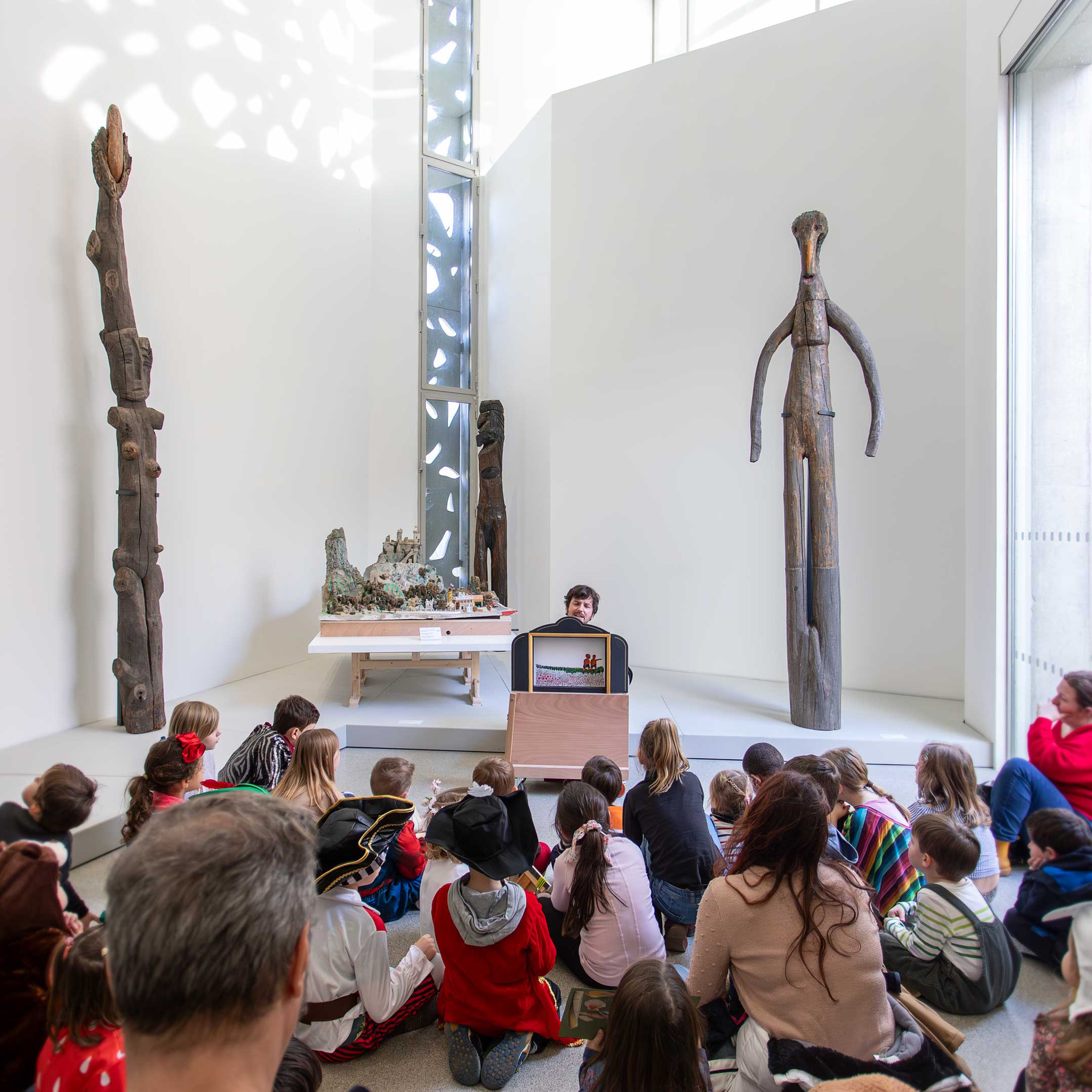 Groupe d'enfants au sol devant un guide qui montre une œuvre, à l'occasion d'un atelier vacances d'été.