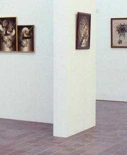 Salle d'exposition présentant des tableaux sur une cimaise et sur le mur.