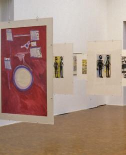 Salle d'exposition avec œuvres graphiques suspendues.