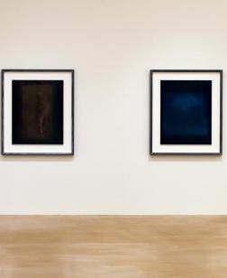 Salle d'exposition avec toiles aux murs foncées.