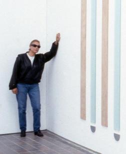 Salle d'exposition avec une œuvre au mur et un homme s'appuyant sur celui-ci.