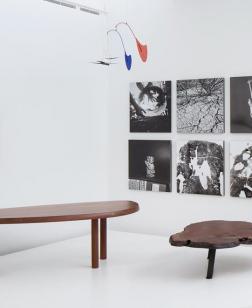Salle d'exposition présentant deux tables en bois, six tableaux en noir et blanc et un mobile de Calder.