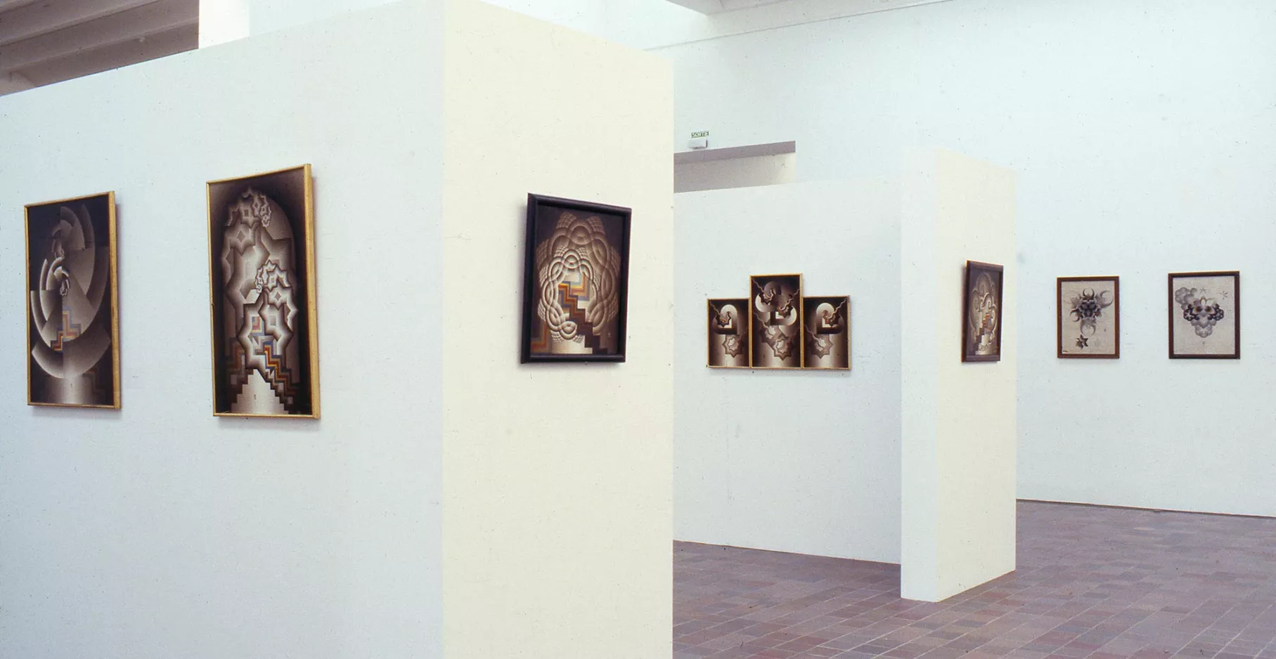 Salle d'exposition présentant des tableaux sur deux cimaises et sur le mur.