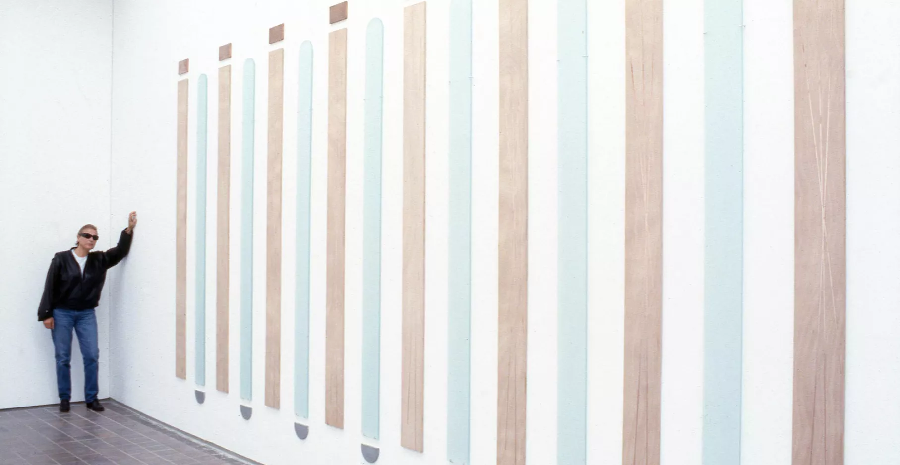 Salle d'exposition avec une œuvre au mur et un homme s'appuyant sur celui-ci.