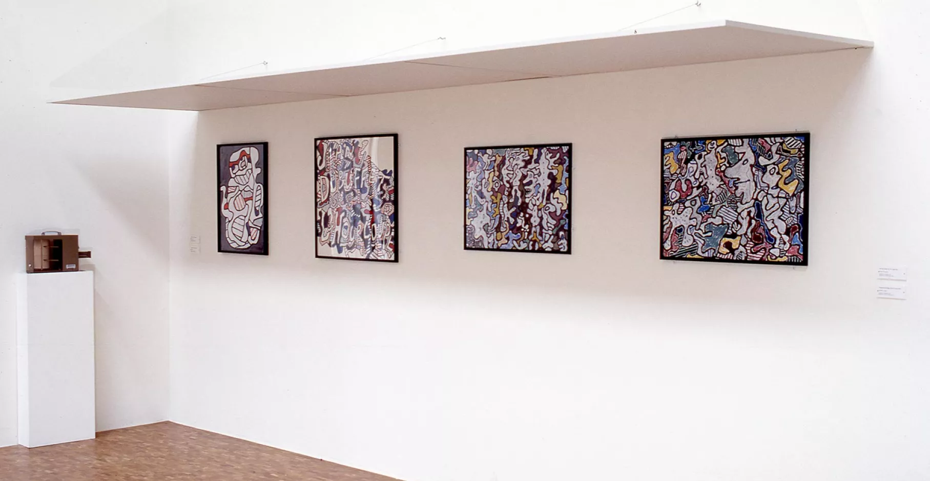 Salle d'exposition avec quatre tableaux au mur.