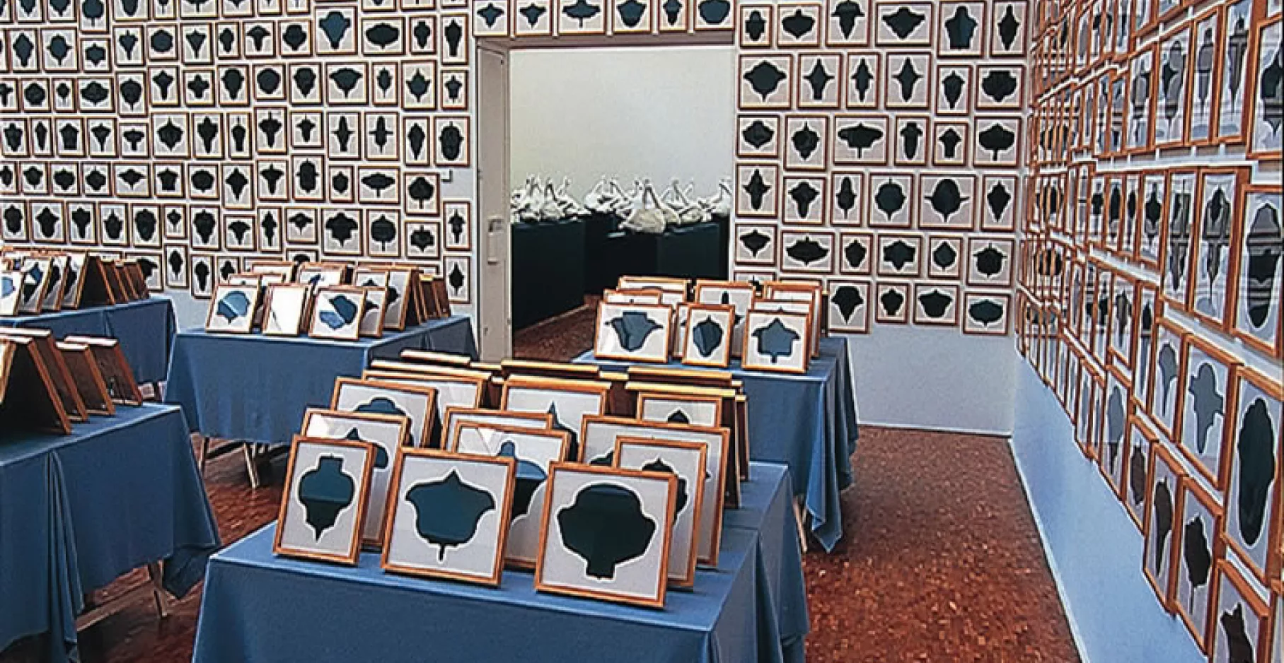 Accumulation de tableaux sur tables et murs d'une salle d'exposition.