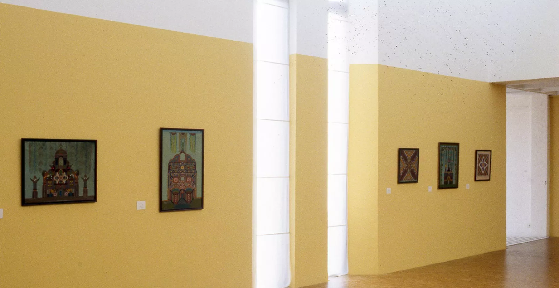 Cinq toiles sur un mur jaune.