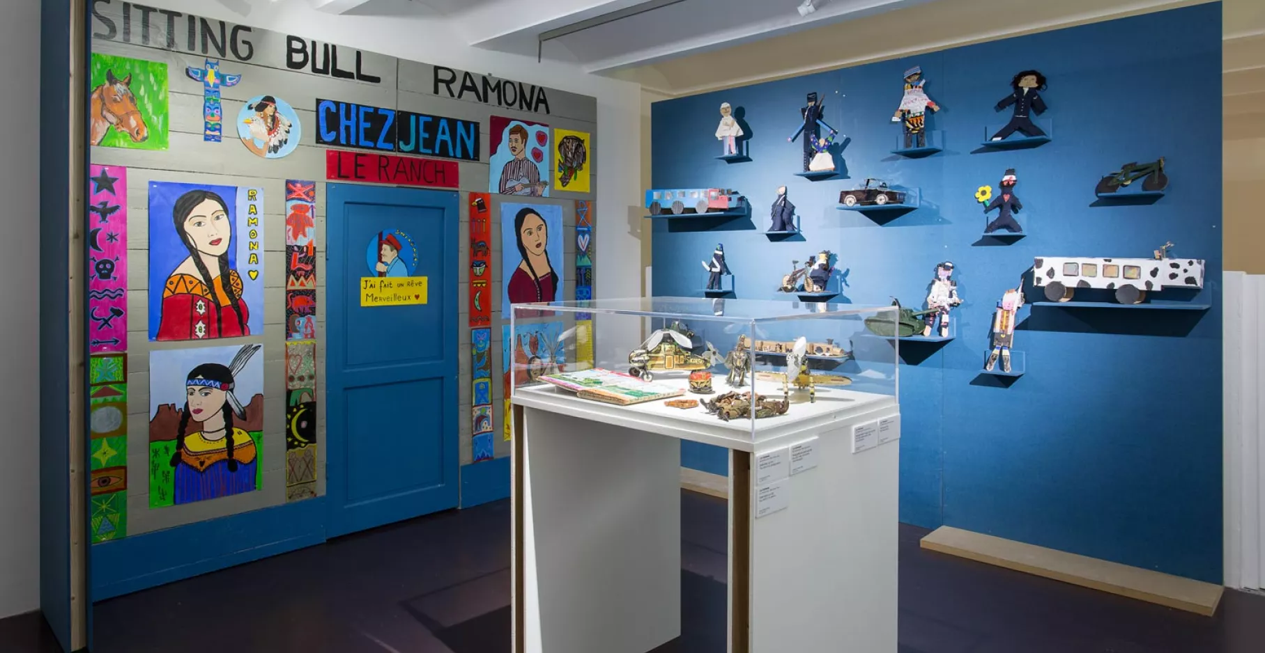 Salle d'exposition avec vitrine en son centre et œuvres aux murs.